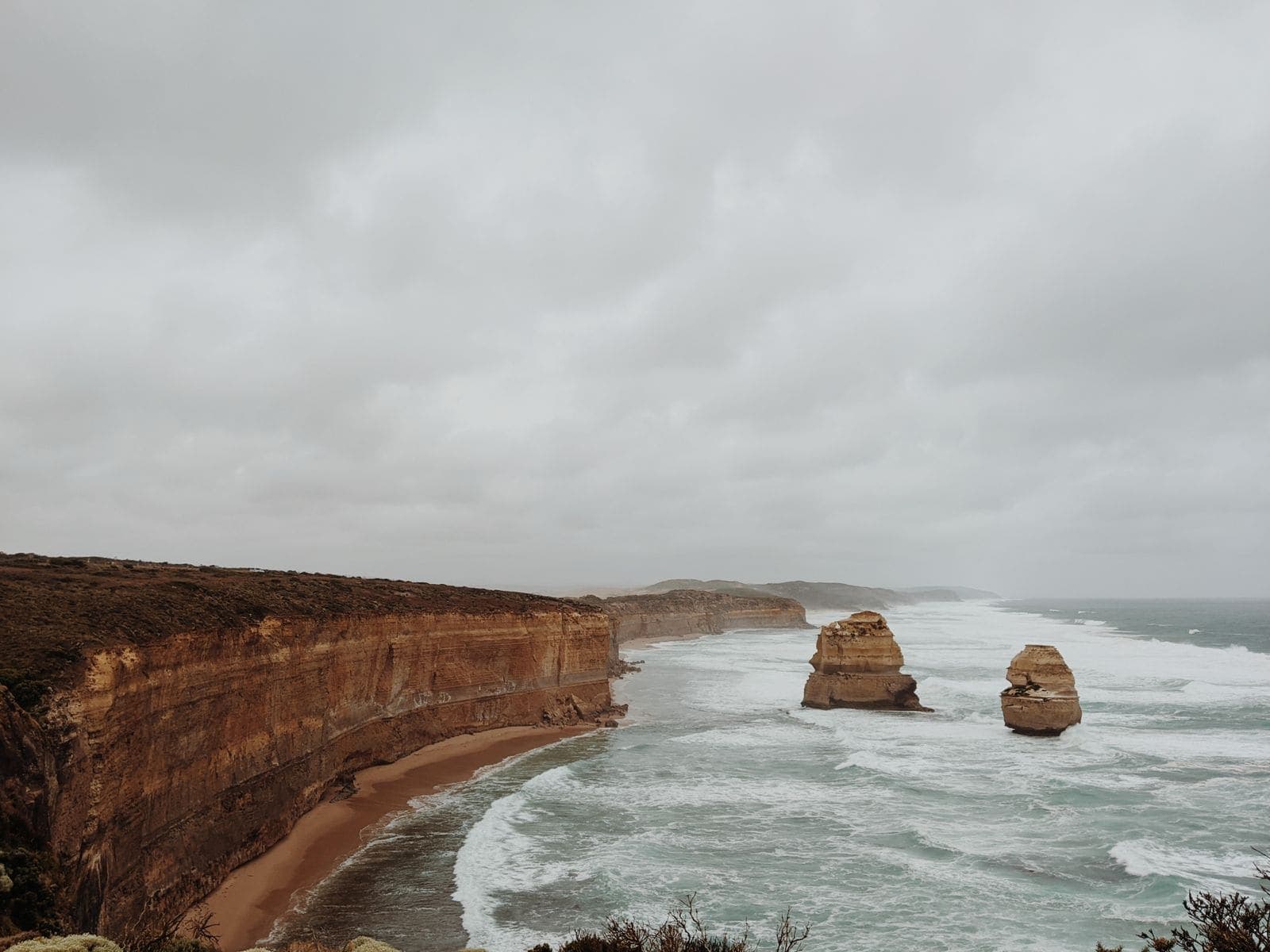 Two limestone stacks standing off a cliff-backed beach under heavy grey cloud