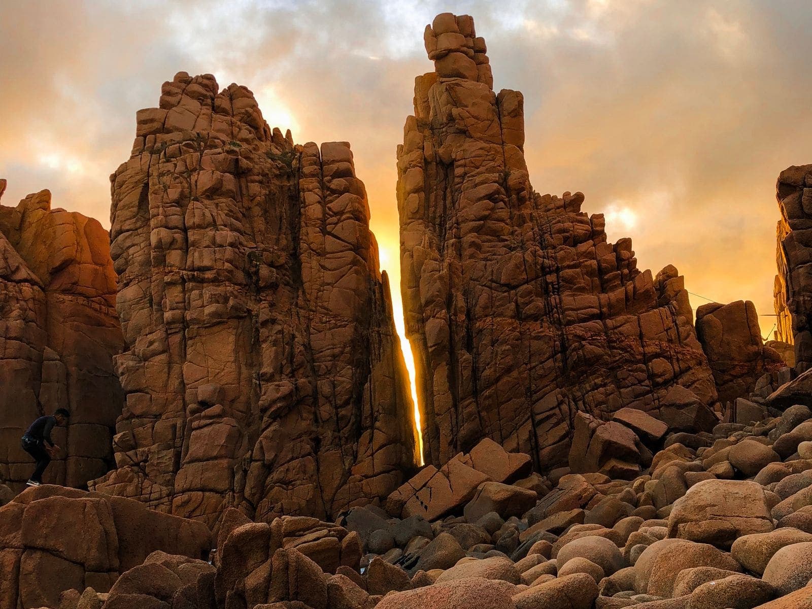 Weathered granite columns catching low golden light above a boulder-strewn shore