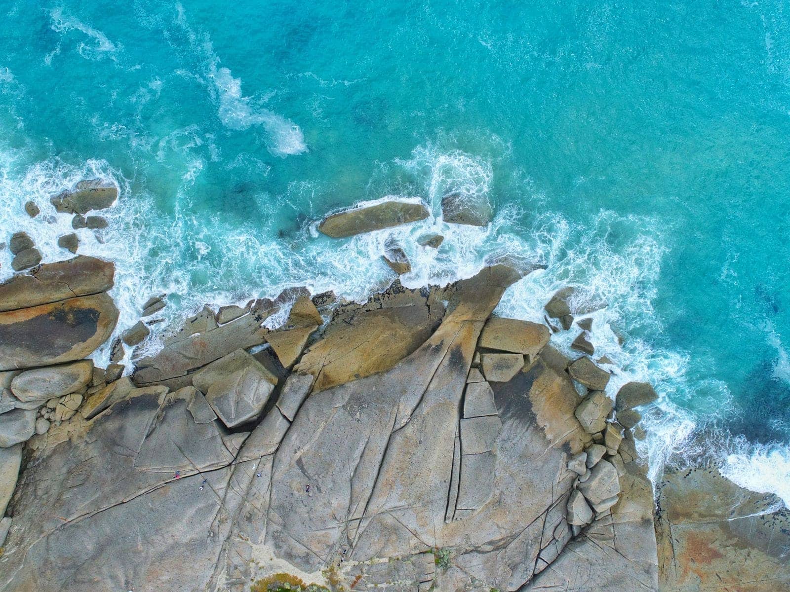 Aerial view of pale granite slabs and boulders meeting brilliant turquoise water