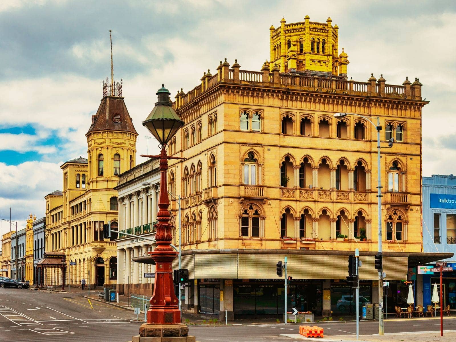 An ornate sandstone Victorian bank building on a corner beside a cast-iron street lamp