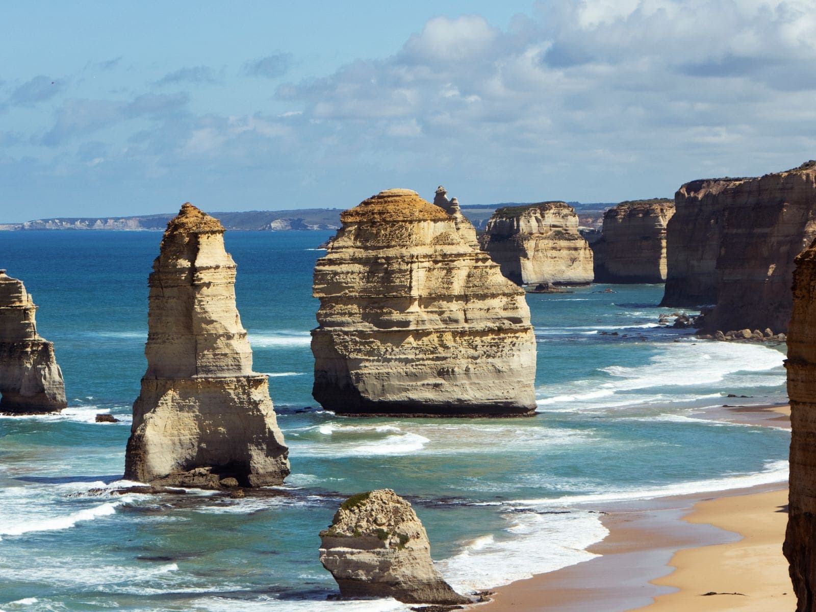 The Twelve Apostles limestone stacks rising from turquoise surf beside a sandy beach and cliffs