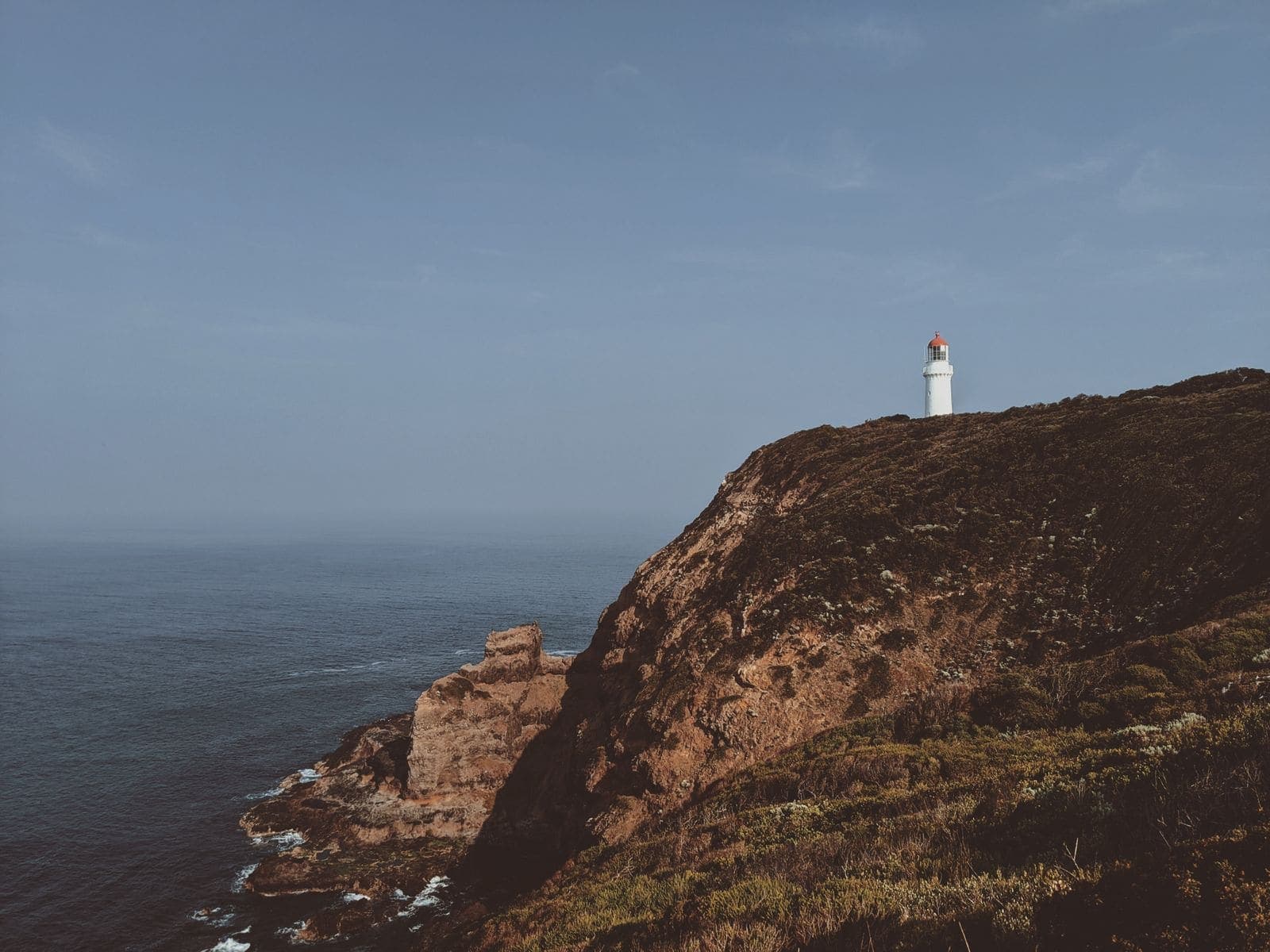 A white lighthouse on a high grassy headland above dark sea cliffs