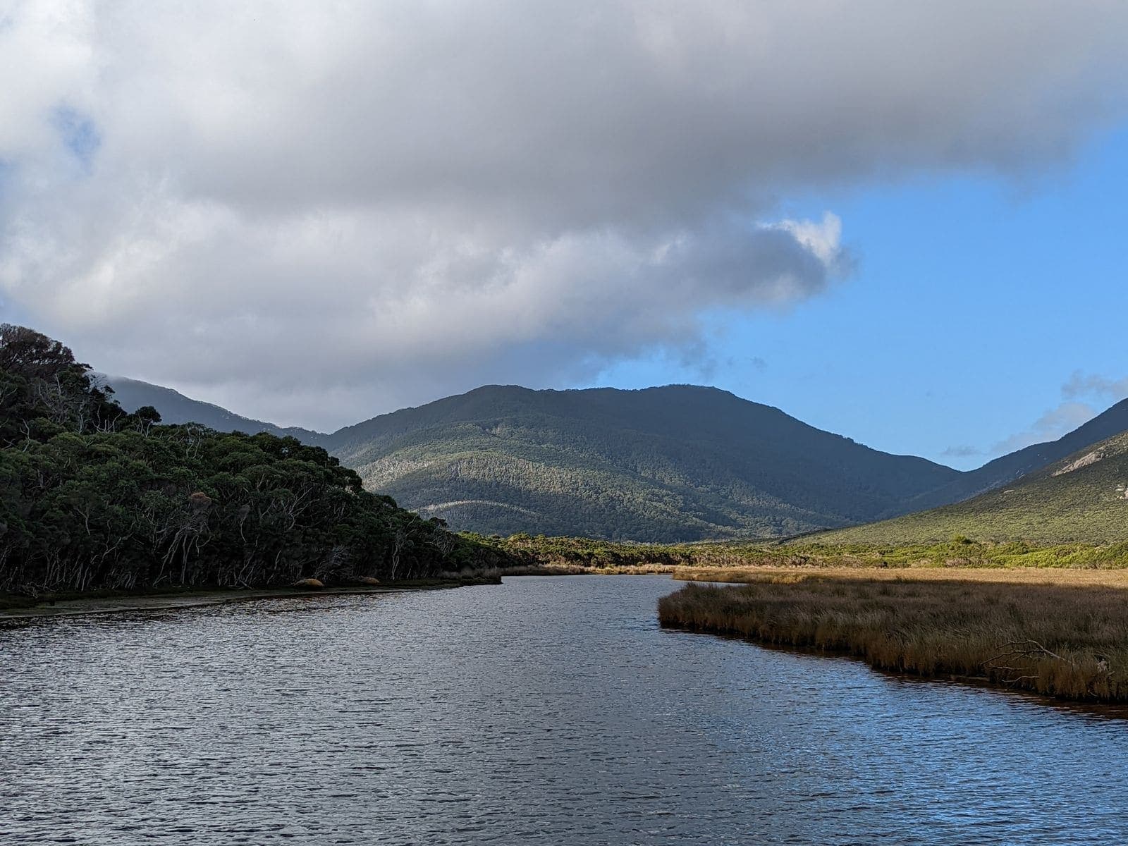 A tidal river winding between low scrub toward rounded green mountains