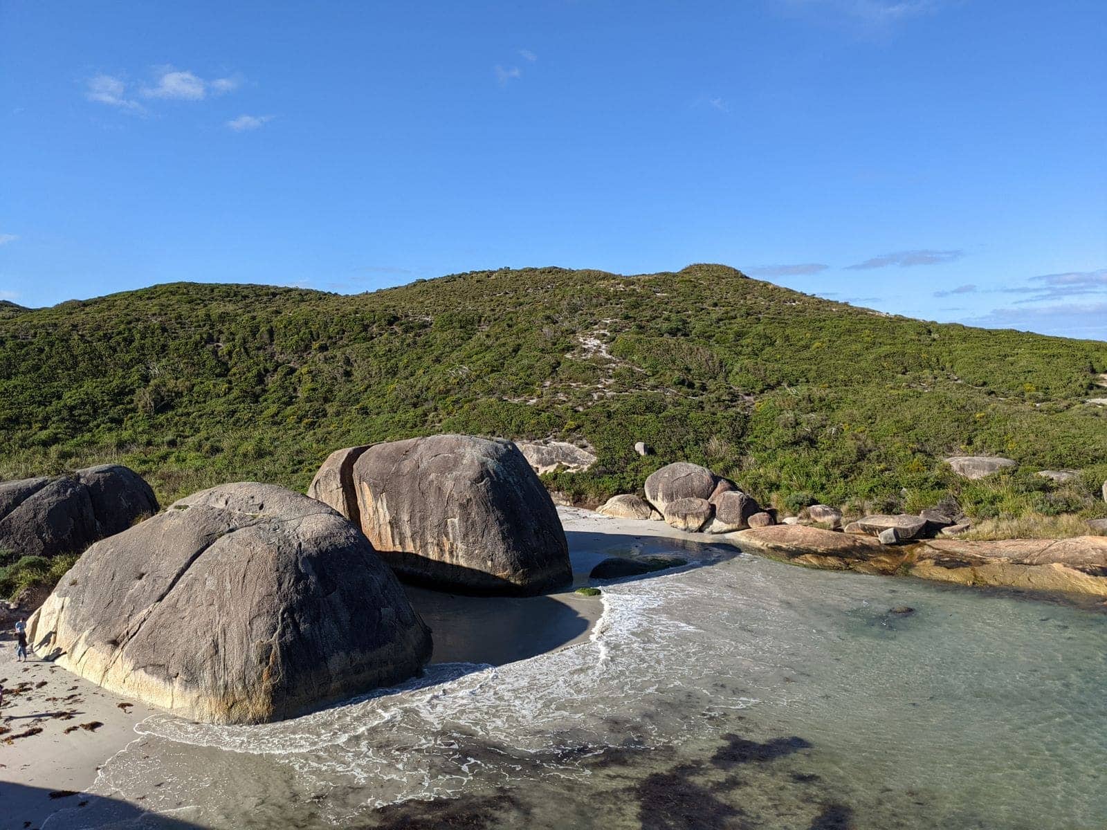 Huge rounded granite boulders sitting on a beach below scrub-covered hills